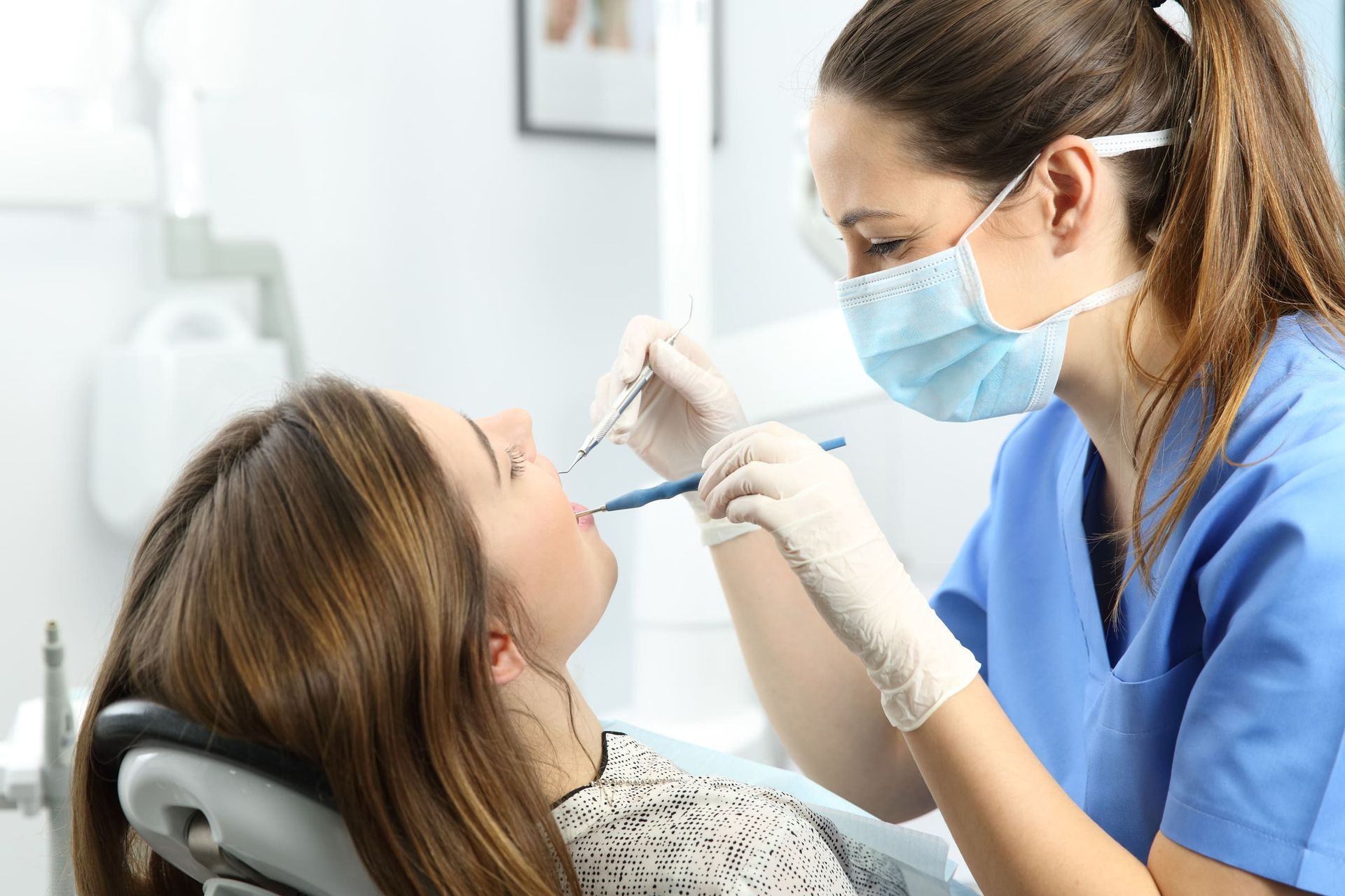 Una mujer está sentada en una silla dental mientras un dentista le examina los dientes.
