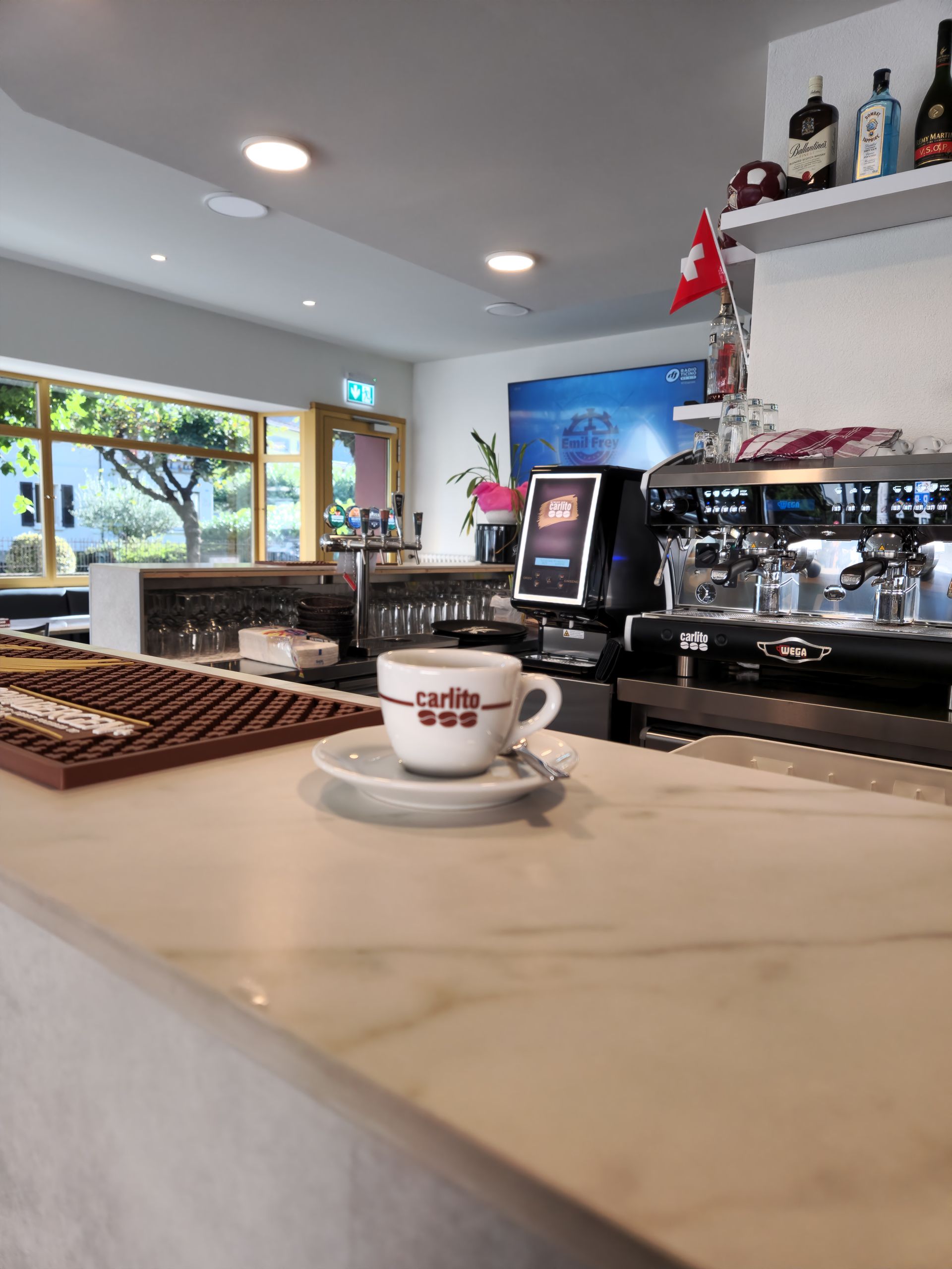 Tazzina da caffè espresso su un bancone di marmo in un bar, con una macchina per il caffè e una finestra sullo sfondo.