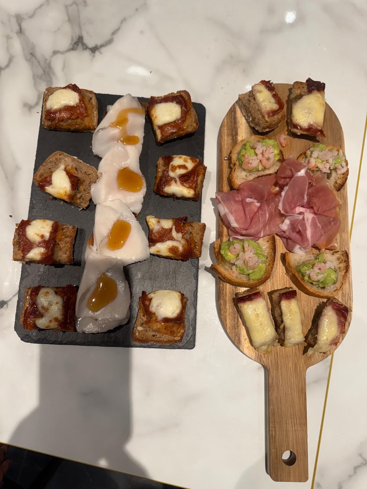 Due taglieri con antipasti: formaggi e salumi su una superficie di marmo.