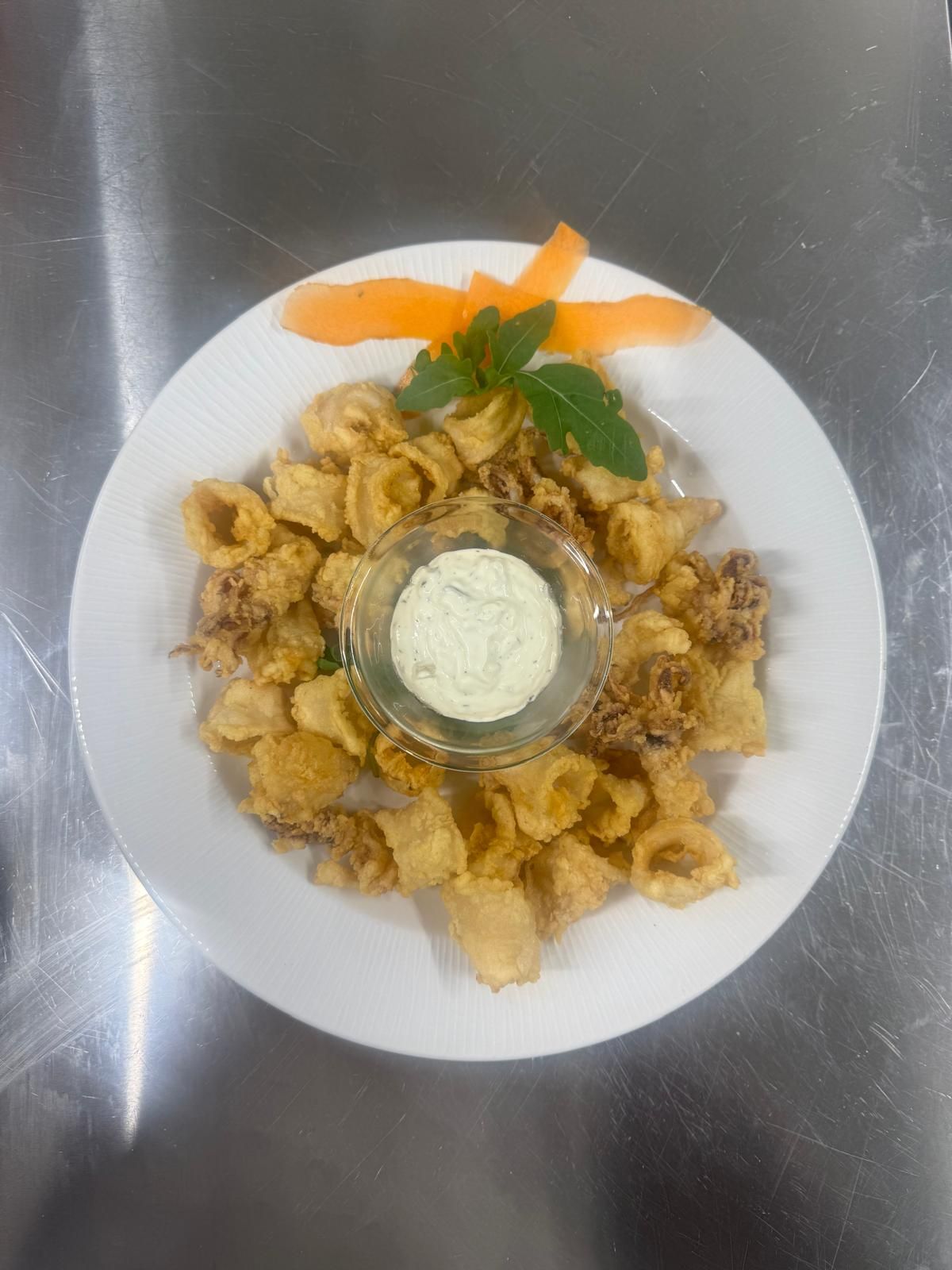 Calamari fritti con salsa, guarnito con carota e rametto di erbe aromatiche su un piatto bianco.