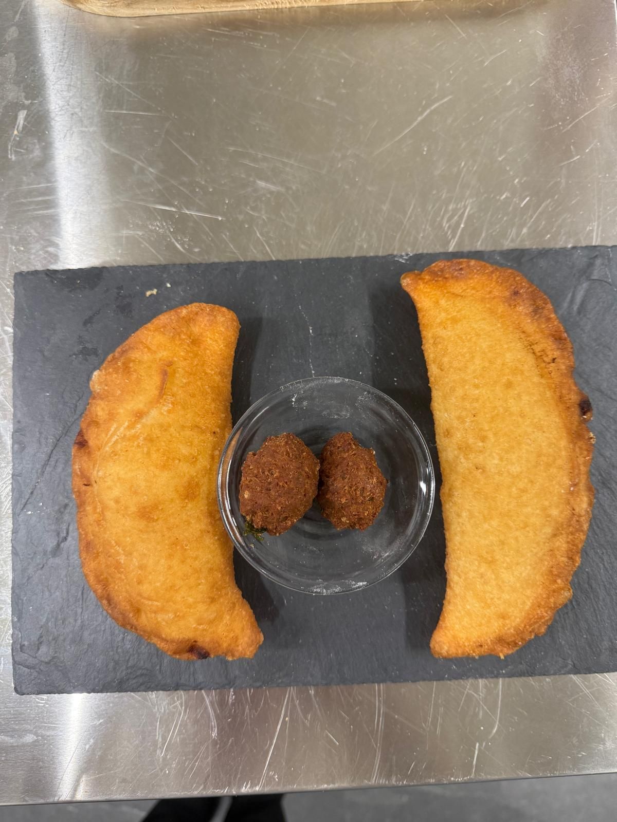 Due empanadas dorate con salsa, servite su una lavagna nera.
