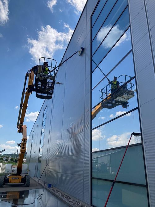 An einem hellen, sonnigen Tag hängt ein Fensterputzer an Sicherheitsseilen an der Glasfassade eines hohen Gebäudes.