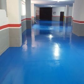 Pasillo vacío con suelo azul brillante y paredes grises con una franja roja