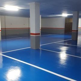 Aparcamiento cubierto vacío con suelo azul brillante, líneas blancas de carril y pilares de hormigón