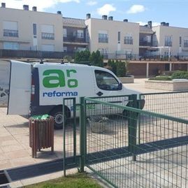 Furgoneta de servicio blanca y verde de Reforma estacionada junto a una acera vallada, frente a unas casas adosadas