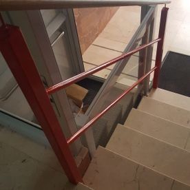 Escalera con barandilla metálica roja junto a unos escalones de baldosas y un rellano con puerta