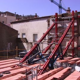 Puntales rojos de acero de un andamio en una obra, junto a la pared de un edificio