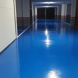 Pasillo vacío con suelo azul brillante y paredes grises, que conduce a unas puertas oscuras al fondo