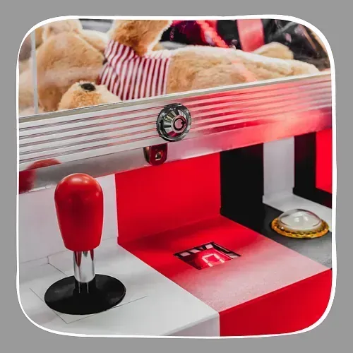 Una máquina arcade roja y blanca con un osito de peluche detrás.