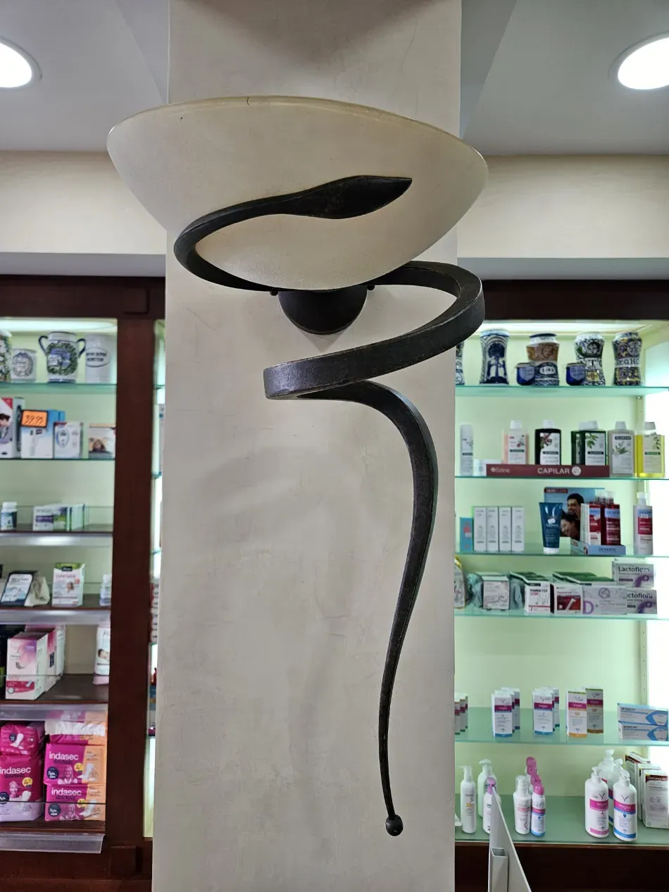 Escultura abstracta en espiral negra bajo un soporte blanco en forma de cuenco en el pasillo de una tienda.