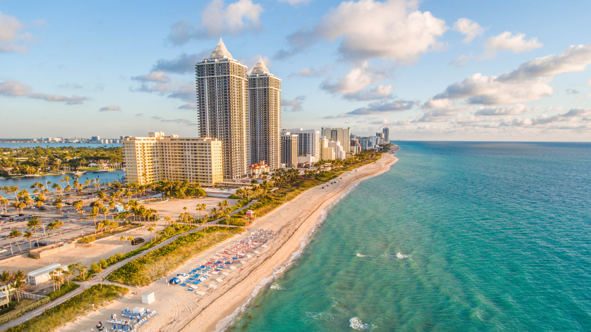 Beachfront view of Miami skyscrapers with turquoise ocean and sandy shore.