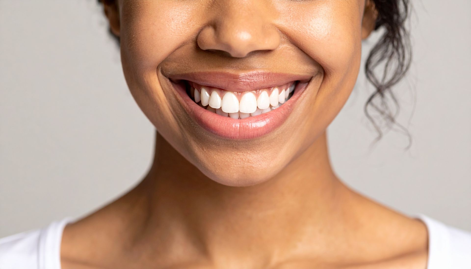 Gros plan sur une bouche souriante et le bas du visage, avec des dents blanches sur fond clair.