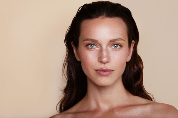 Portrait d'une femme aux cheveux foncés sur fond beige uni, regardant directement l'objectif de l'appareil photo.