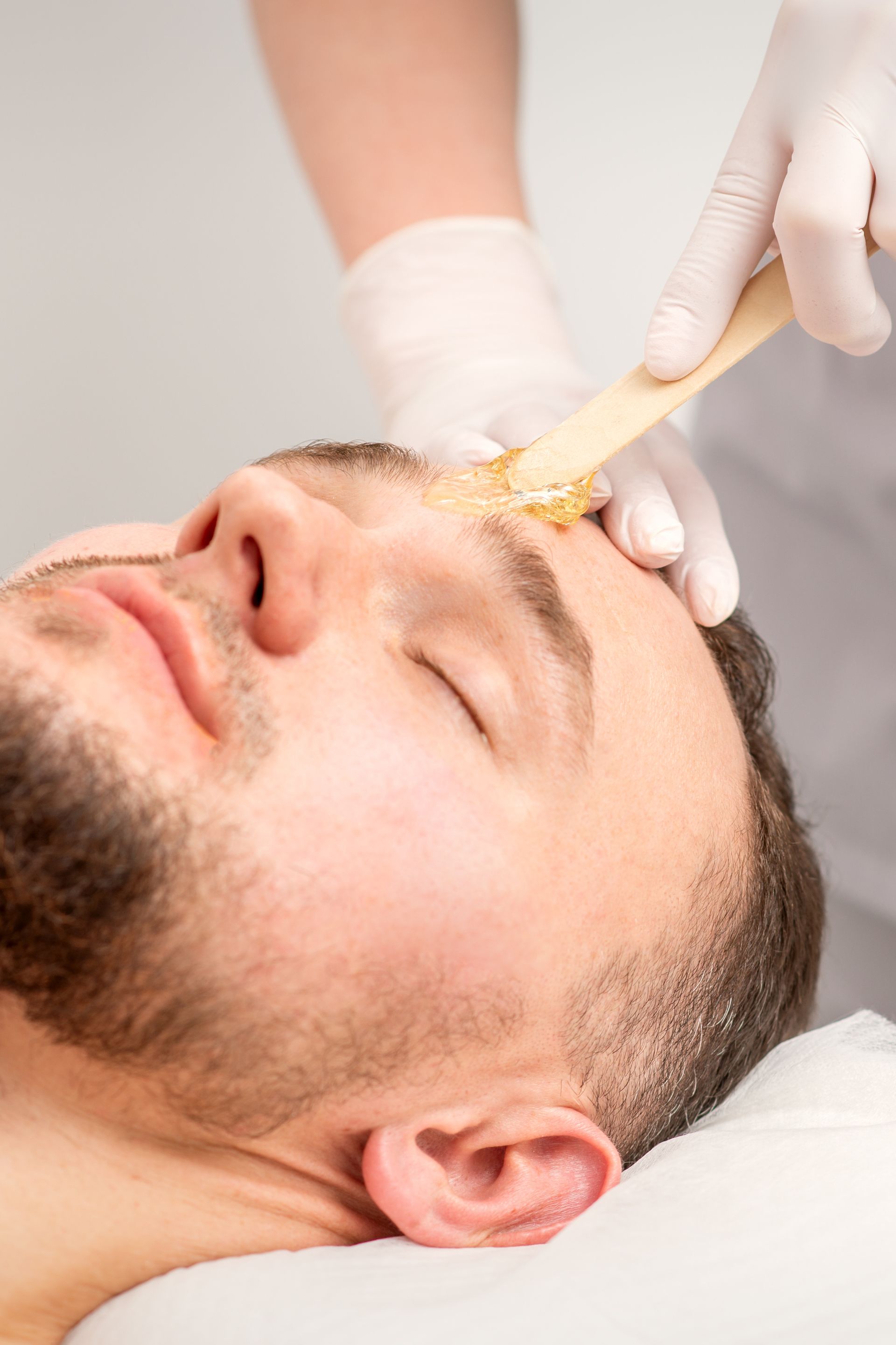 Des mains gantées appliquent un soin du visage à un homme allongé sur un lit de spa.