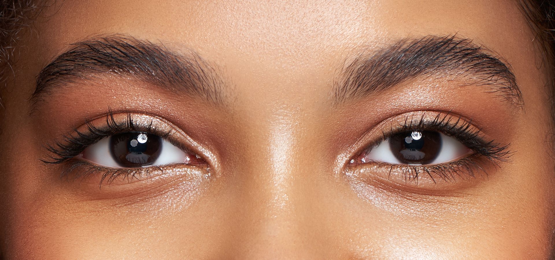 Gros plan sur les yeux d'une personne avec un maquillage léger et des reflets pailletés sur la peau.