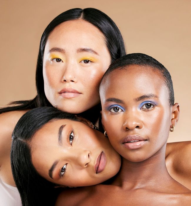 Trois personnes posant côte à côte, arborant un maquillage des yeux coloré, sur un fond beige chaud.