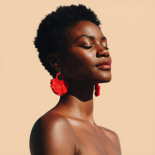 Portrait de profil d'une personne portant des boucles d'oreilles rouges sur fond pêche.