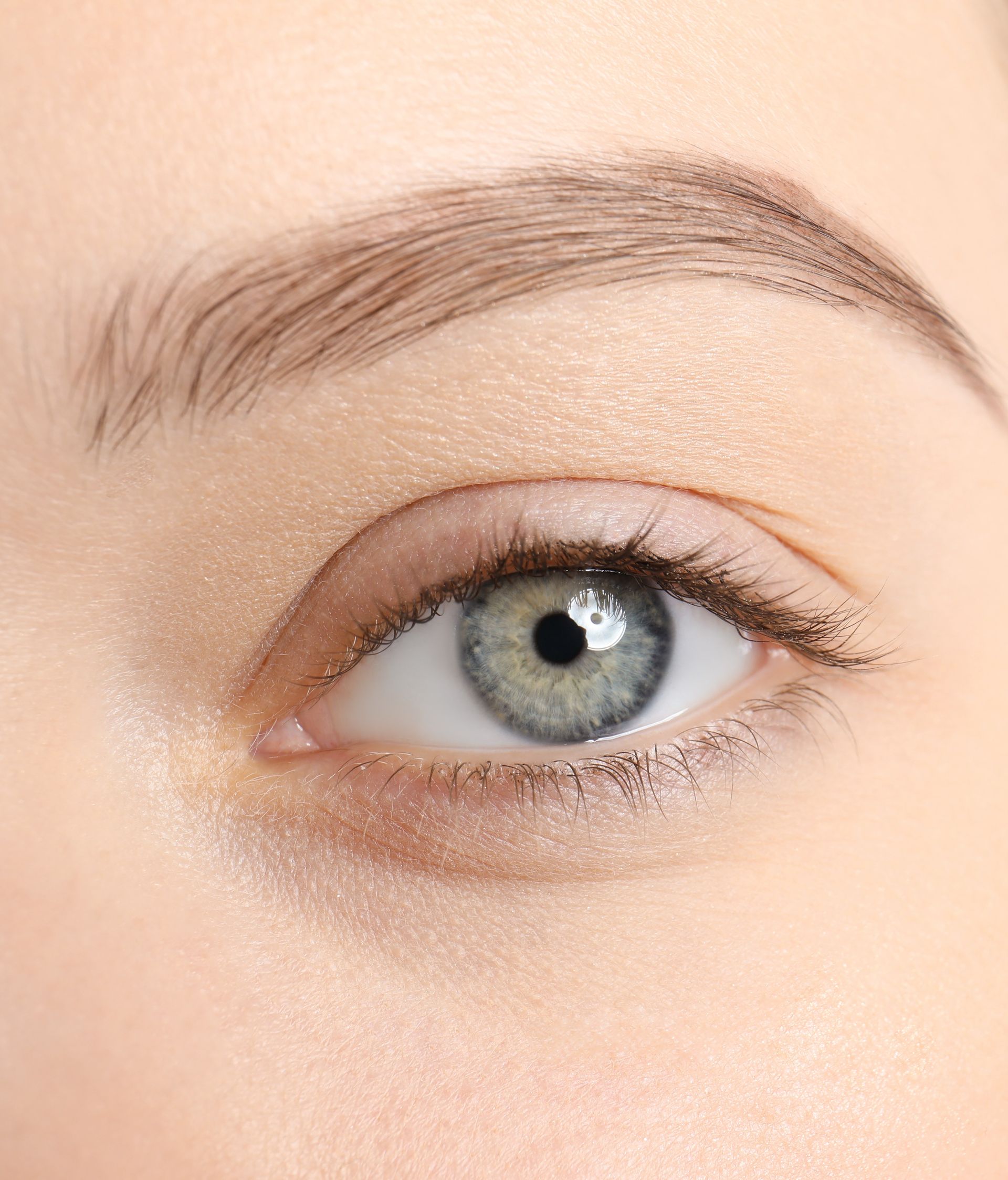 Gros plan sur un œil bleu-vert unique, avec un sourcil dessiné et un maquillage léger.