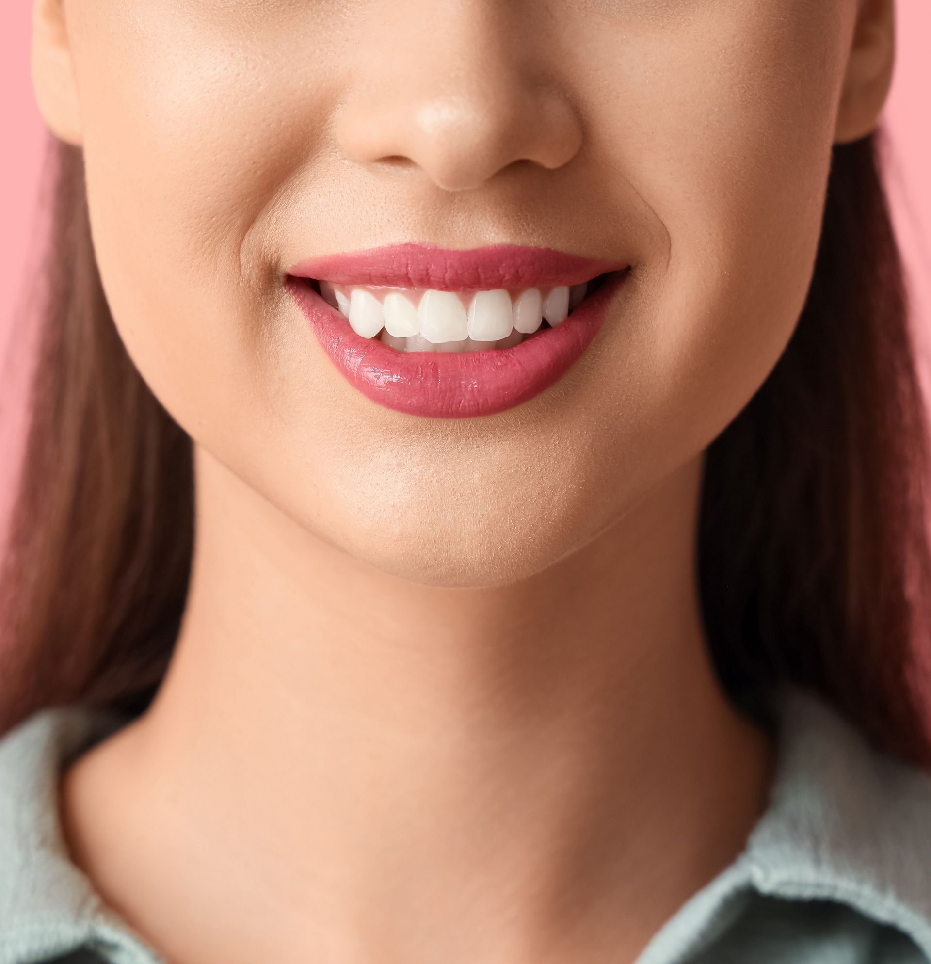 Gros plan sur une personne souriante aux lèvres roses brillantes et portant une chemise bleu clair à col.
