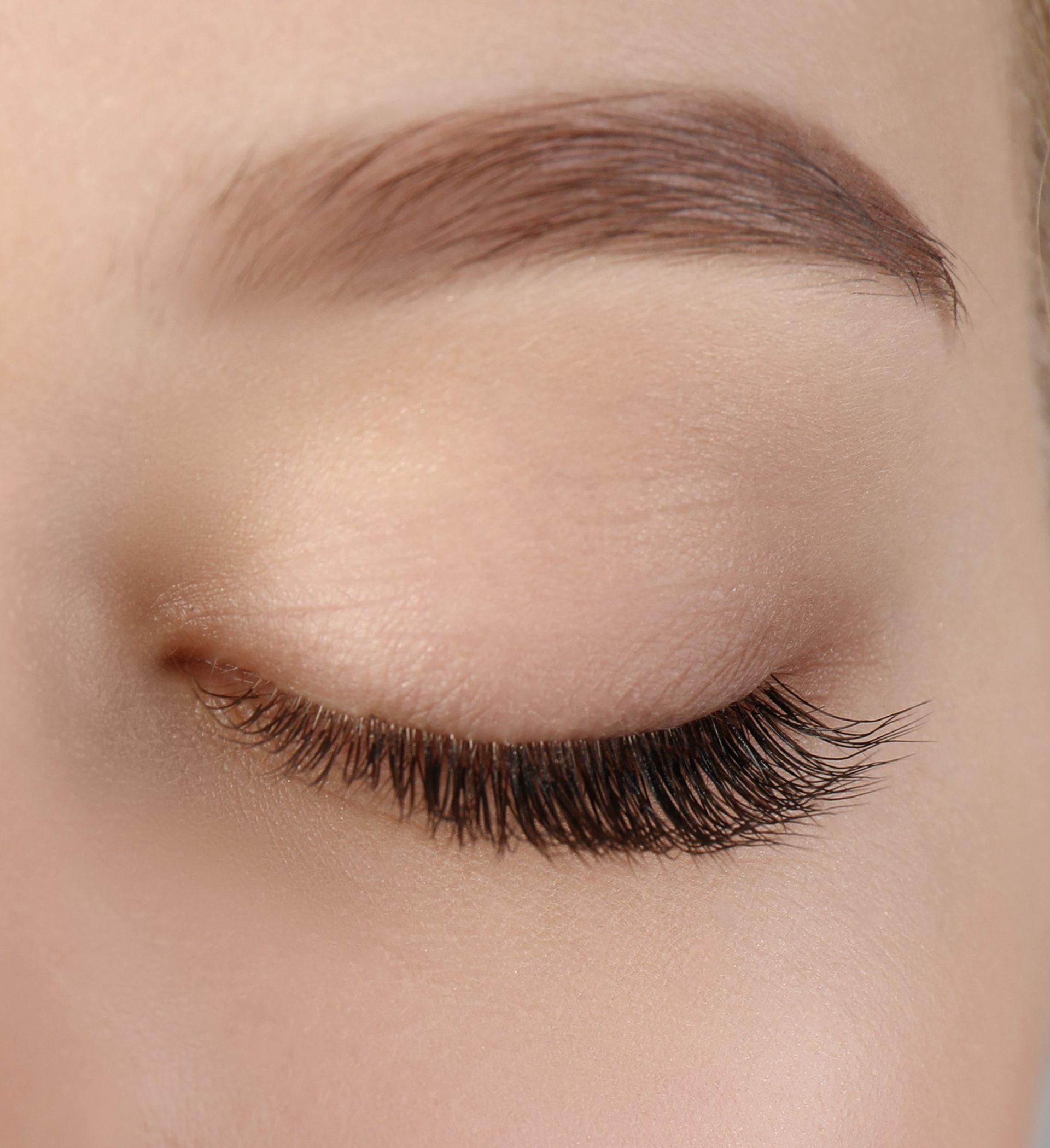 Œil fermé avec de longs faux cils et un sourcil brun bien dessiné sur un fond neutre.