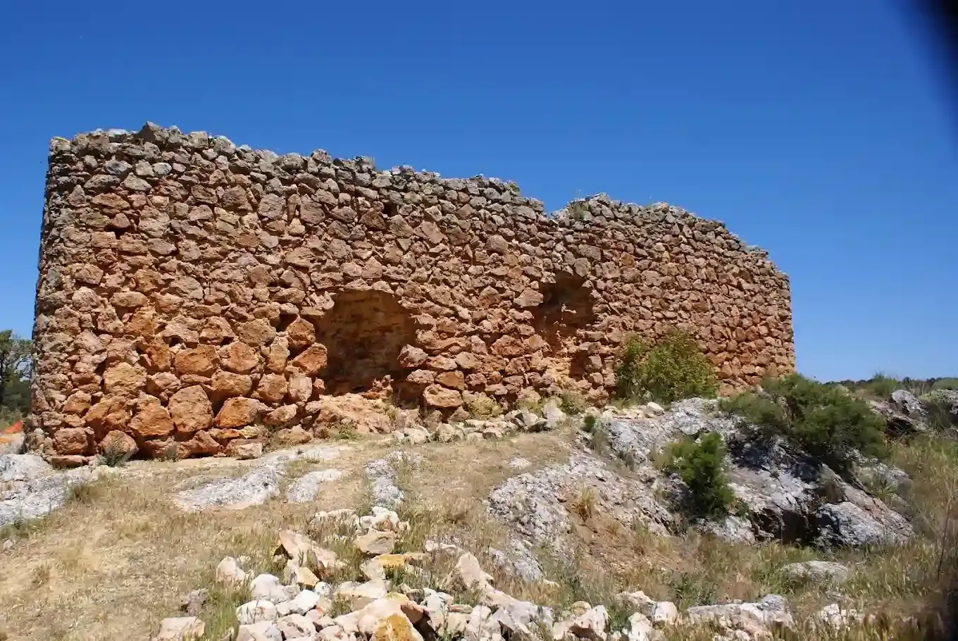 Estructura de piedra en ruinas sobre una colina, piedras marrones, fondo de cielo azul.