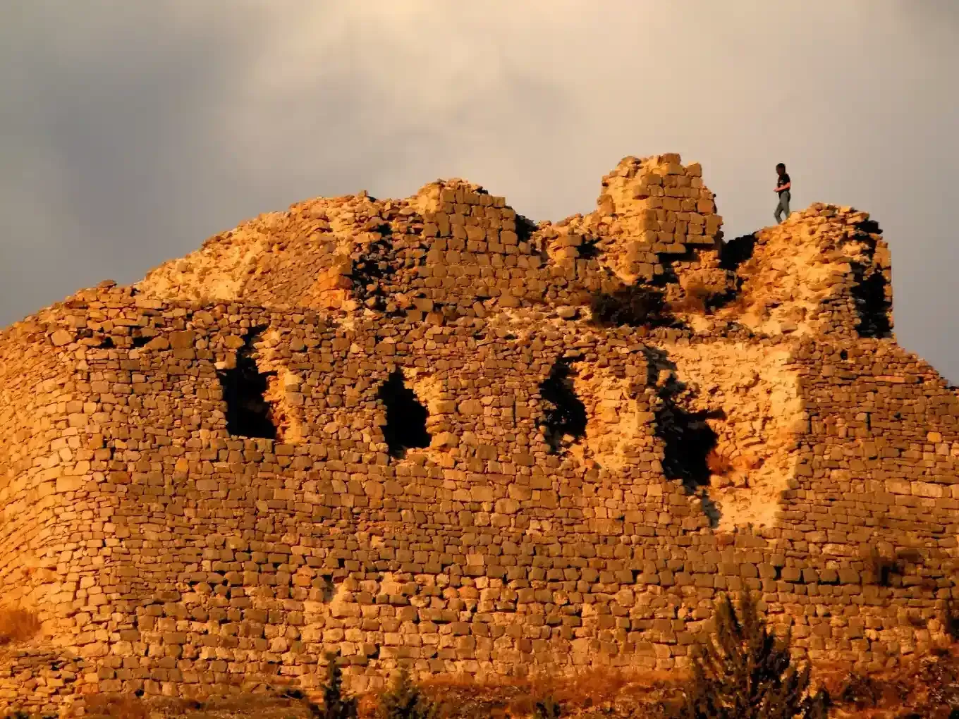 Estructura de castillo de piedra en ruinas con un arquero recortado en la cima.