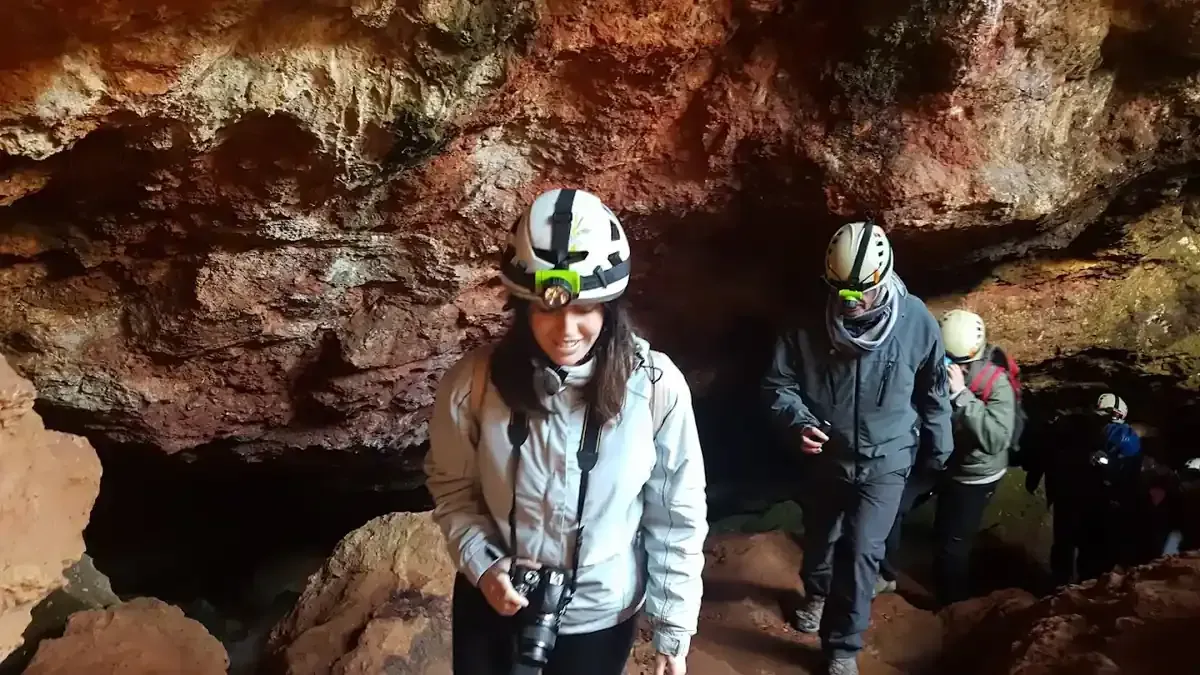 Personas con cascos y linternas frontales exploran una cueva con paredes de color marrón rojizo.