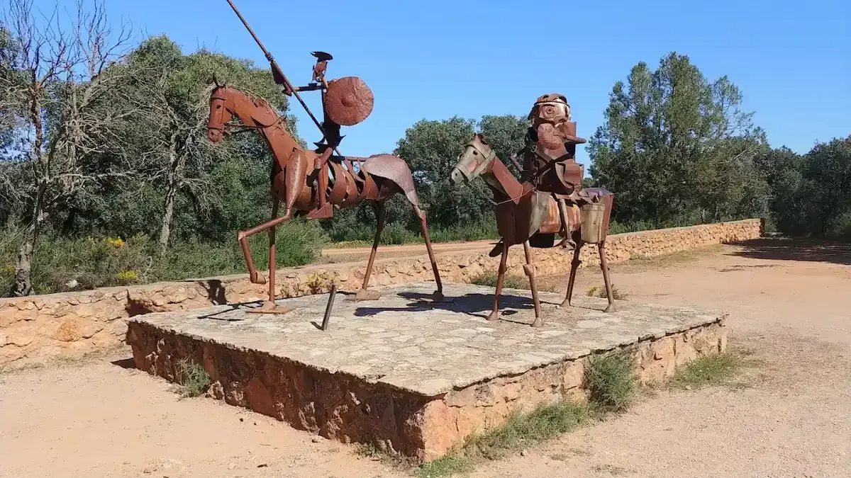 Escultura metálica de Don Quijote y Sancho Panza a caballo, al aire libre sobre plataforma de piedra.