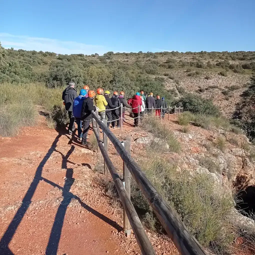 Un grupo que usa cascos camina por un sendero al lado de un cañón de roca roja.