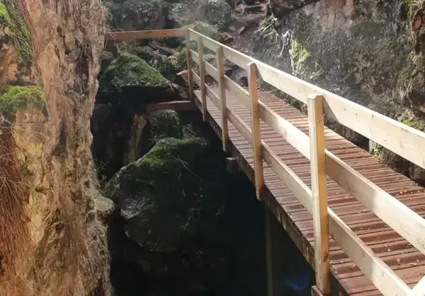 Puente de madera sobre un profundo desfiladero rocoso. Rocas cubiertas de musgo bordean las paredes.