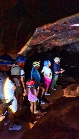 Personas con linternas frontales en una cueva, observando algo. Interior oscuro, con formaciones rocosas visibles.