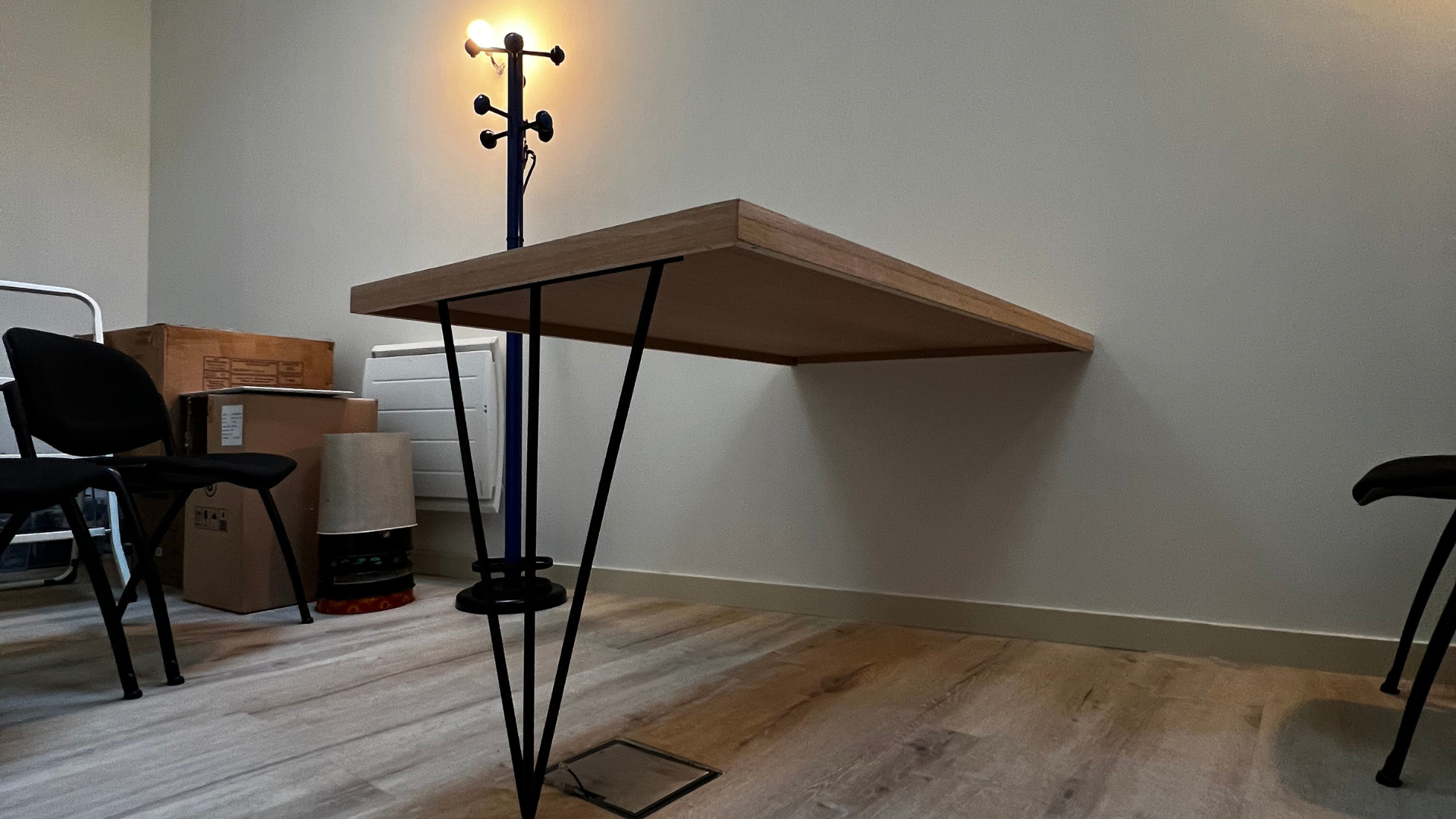 Une table avec des pieds en épingle à cheveux est posée sur un plancher en bois dans une pièce.