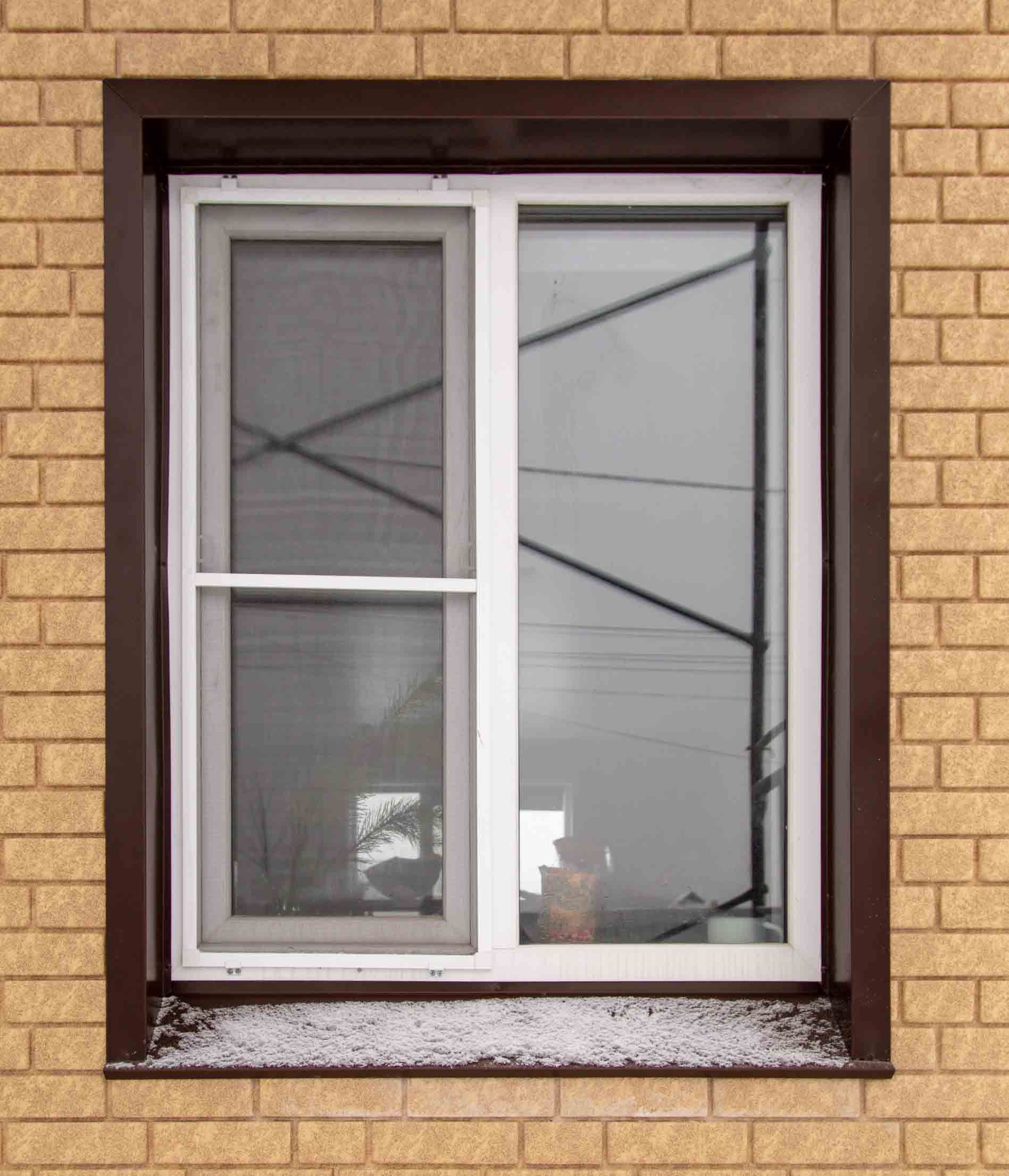 Una ventana con una mosquitera está en una pared de ladrillos.