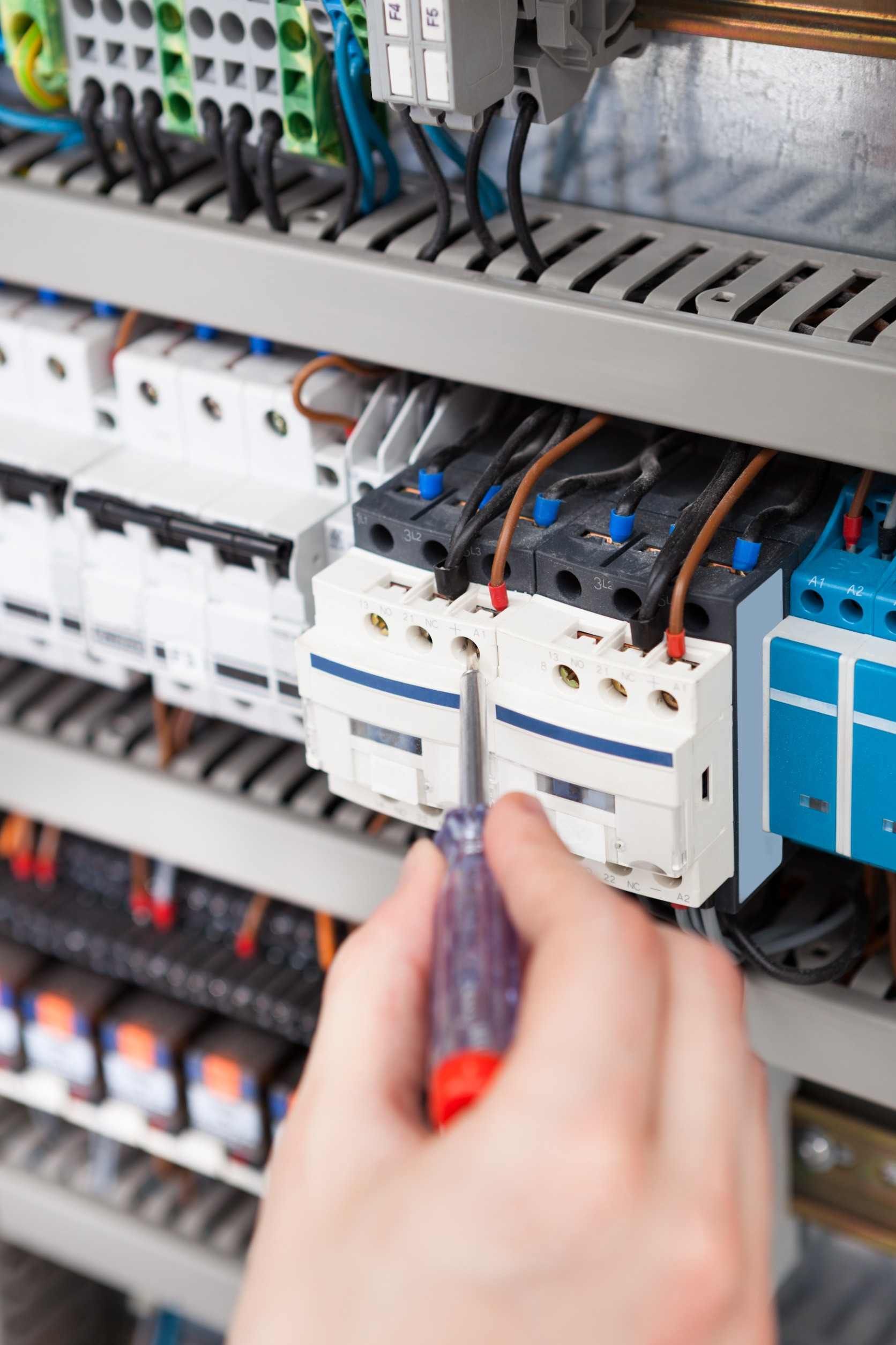 Una persona está trabajando en un panel eléctrico con un destornillador.