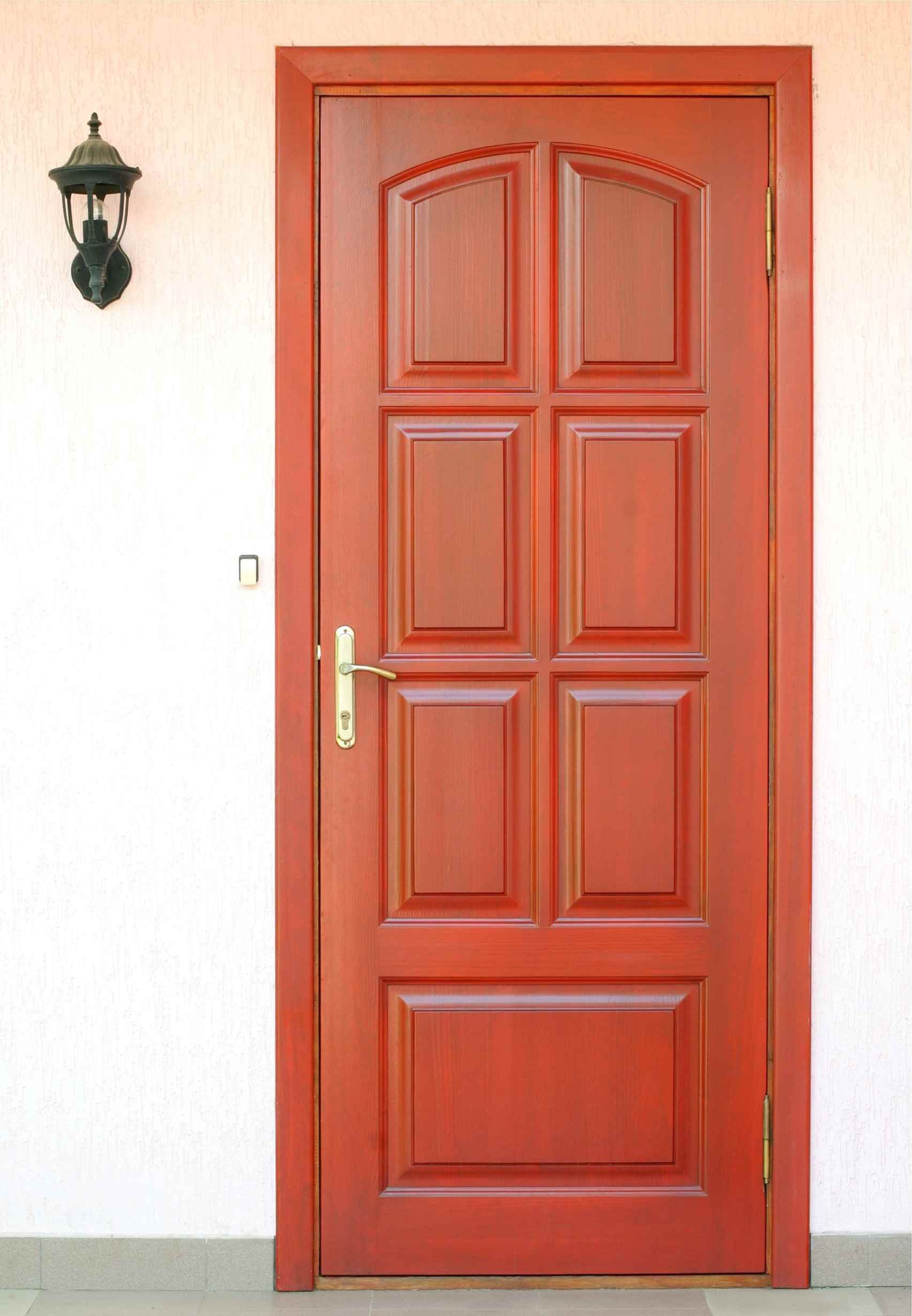 Una puerta de madera roja está contra una pared blanca.
