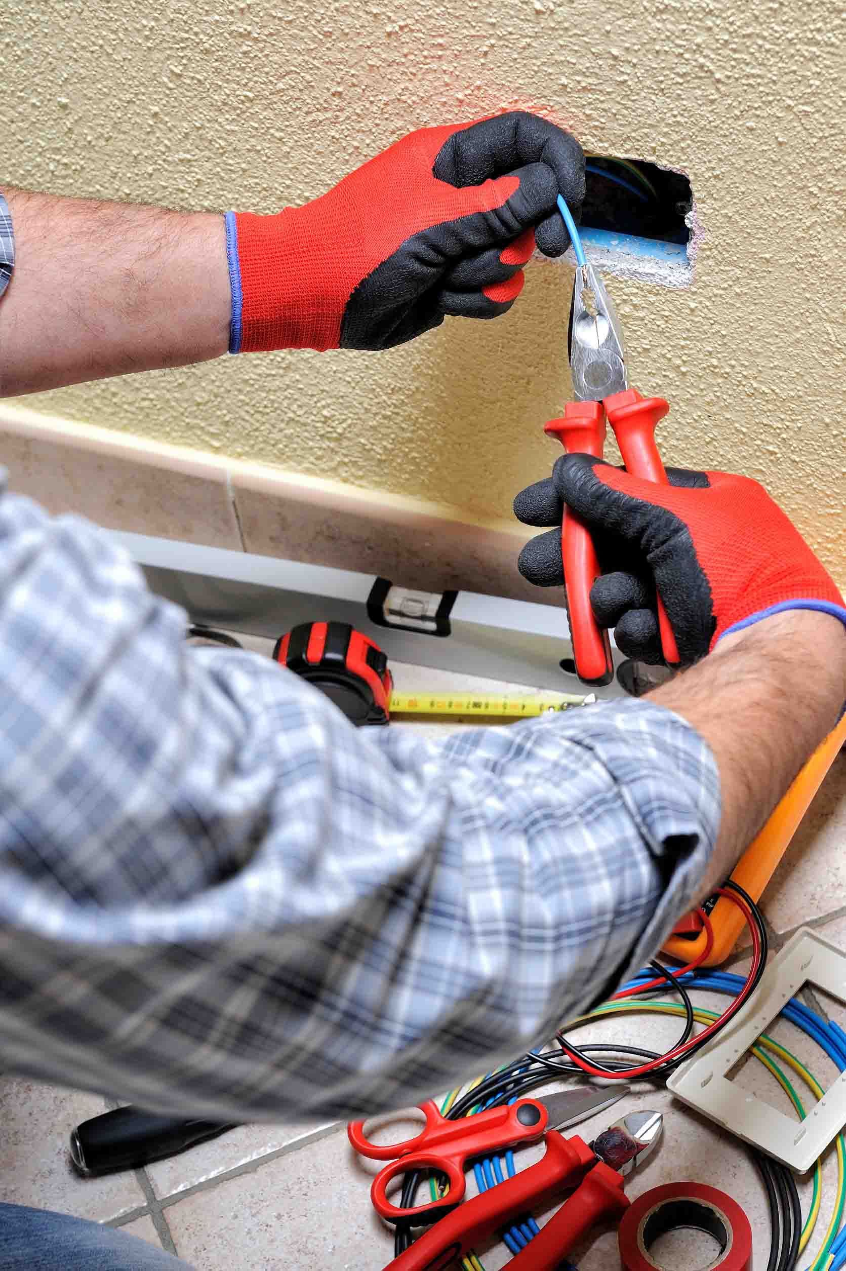 Un hombre que lleva guantes rojos está trabajando con cables eléctricos.