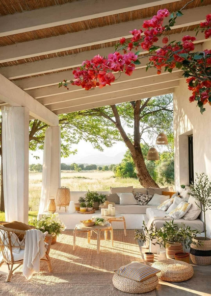 Porche cubierto con asientos al aire libre, enredaderas en flor y vista a un campo.