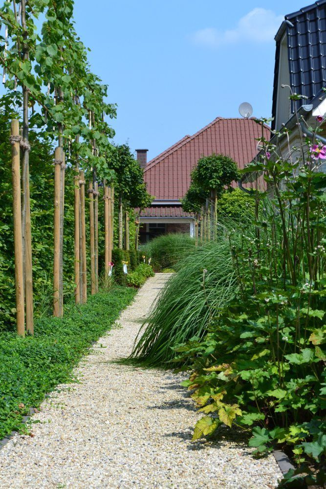 Ein Kiesweg führt zu einem von Bäumen und Büschen umgebenen Haus.