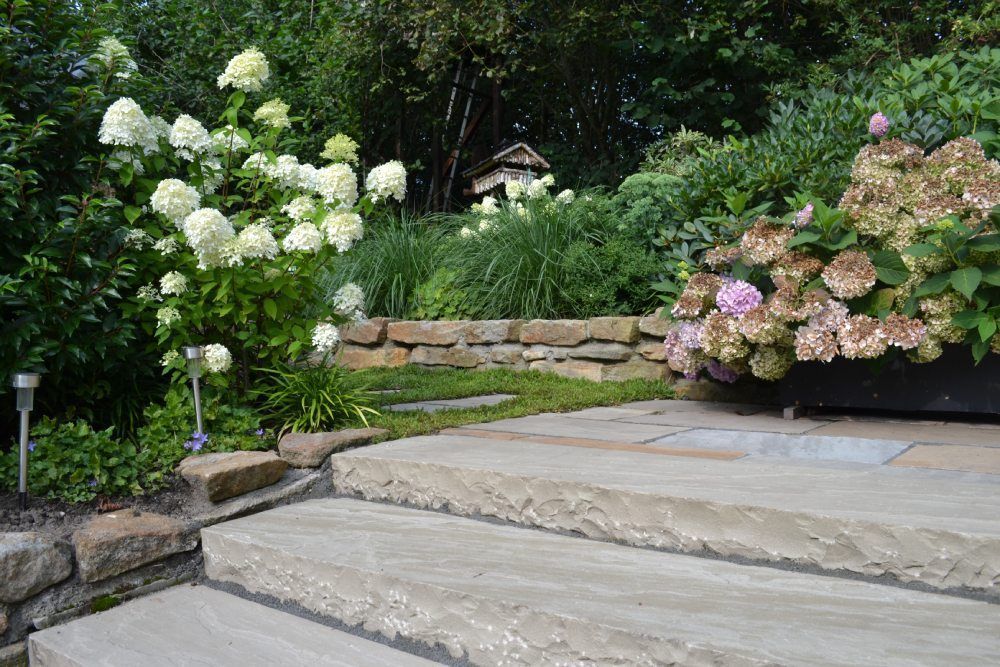 Ein Steinweg führt zu einem Garten mit Blumen und einer Steinmauer.