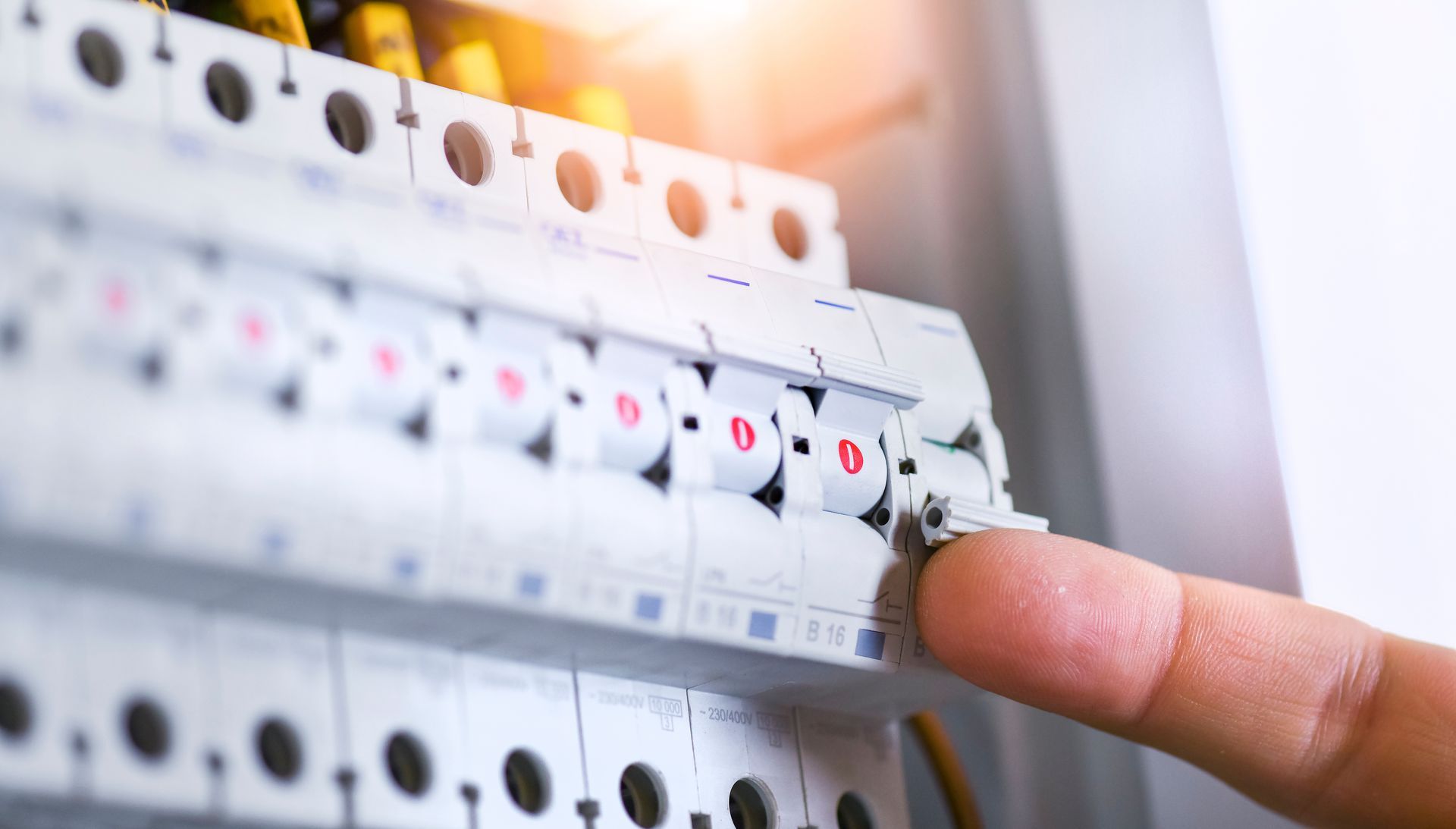 Le doigt d'une personne actionnant un interrupteur sur un tableau électrique résidentiel blanc.