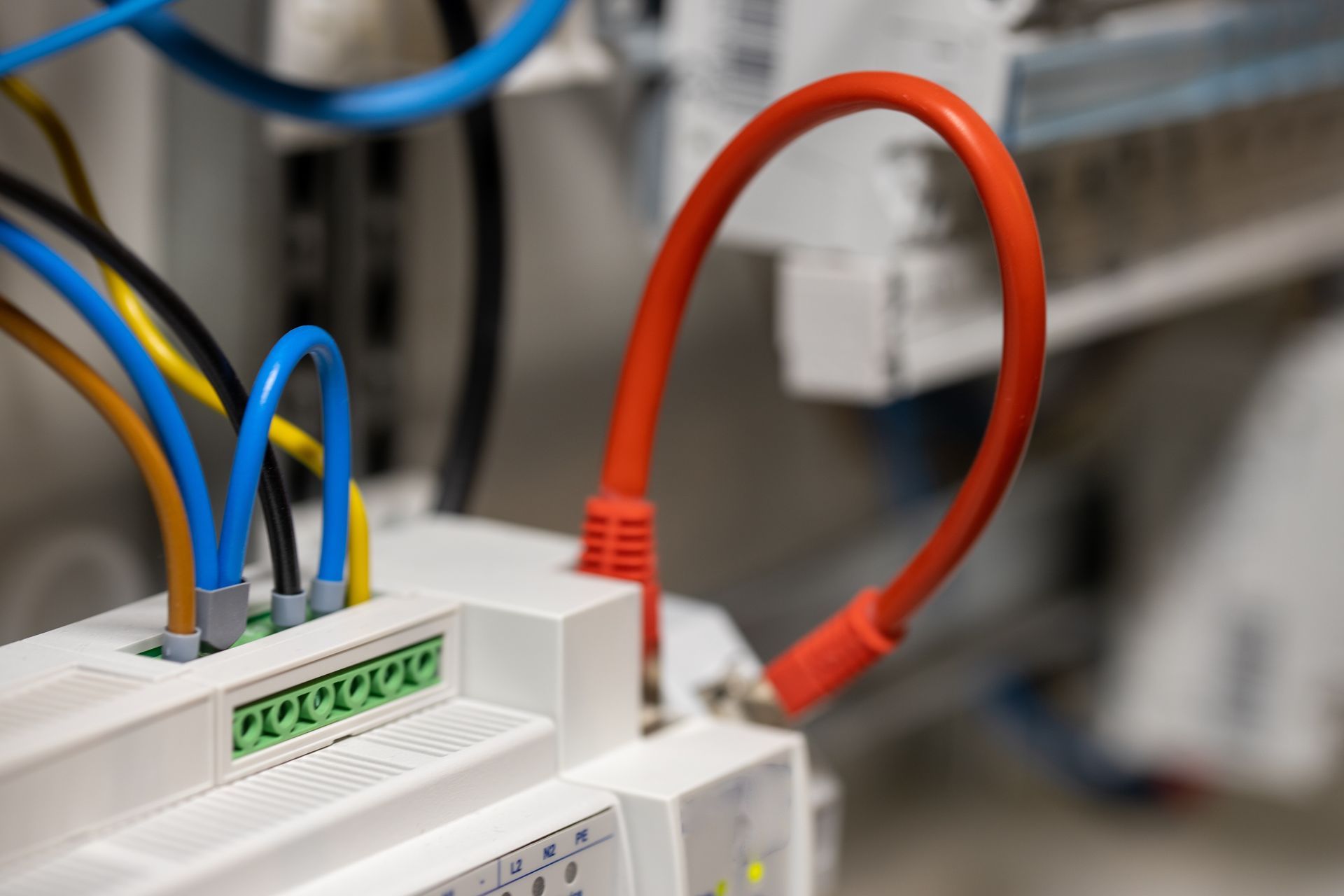 Gros plan sur un module de commande industriel blanc avec plusieurs fils de couleurs différentes connectés à une borne verte et à un câble rouge.