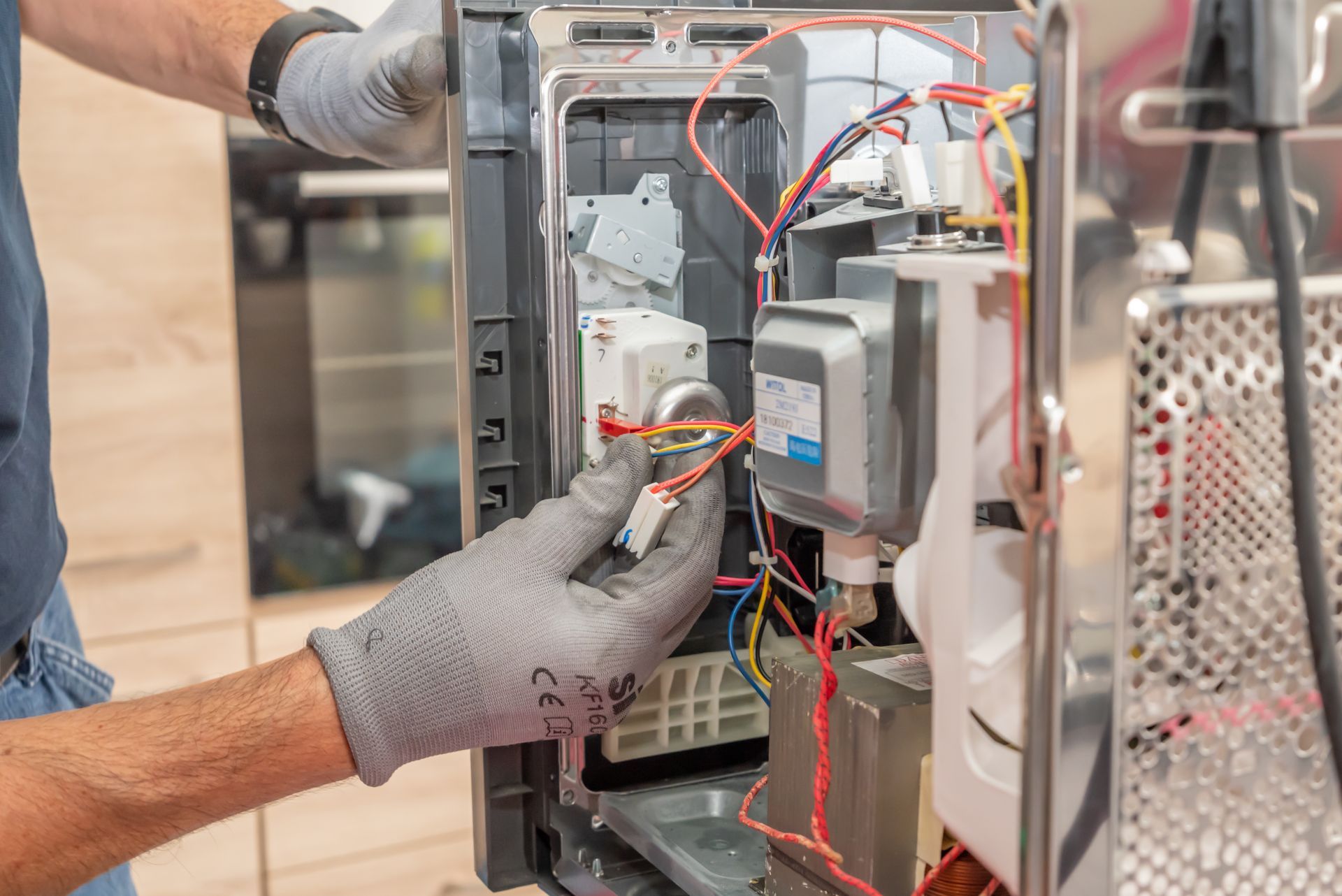 Un technicien portant des gants de travail répare les composants électriques internes d'un four à micro-ondes ouvert.