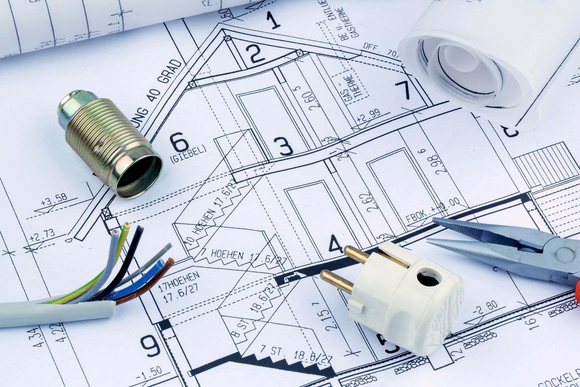 Des outils et des composants de câblage électrique, y compris une prise et un fil, reposent sur un plan de maison.