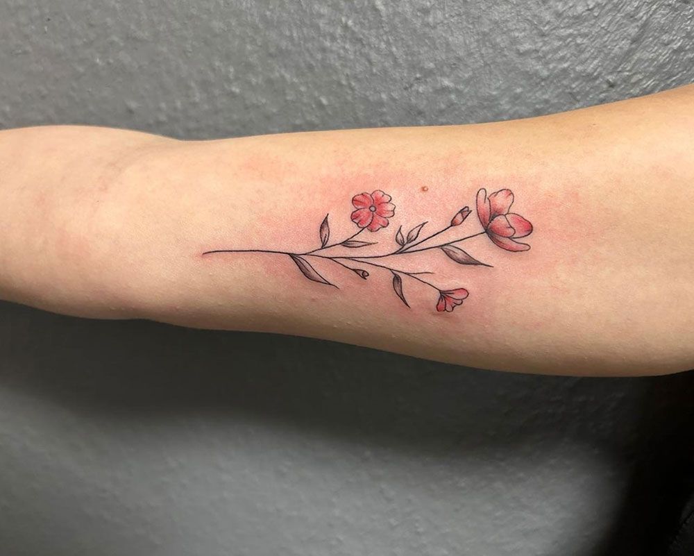 Eine Frau hat eine Tätowierung einer roten Blume auf ihrem Unterarm.