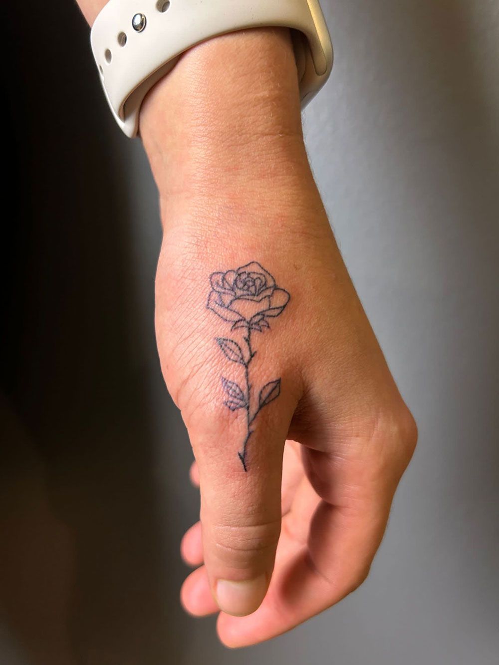 Eine Person hat eine kleine Tätowierung einer Rose auf der Hand