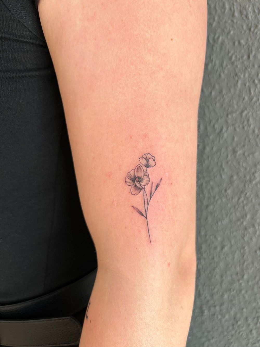 Eine Frau hat eine kleine Blumentätowierung auf ihrem Arm.