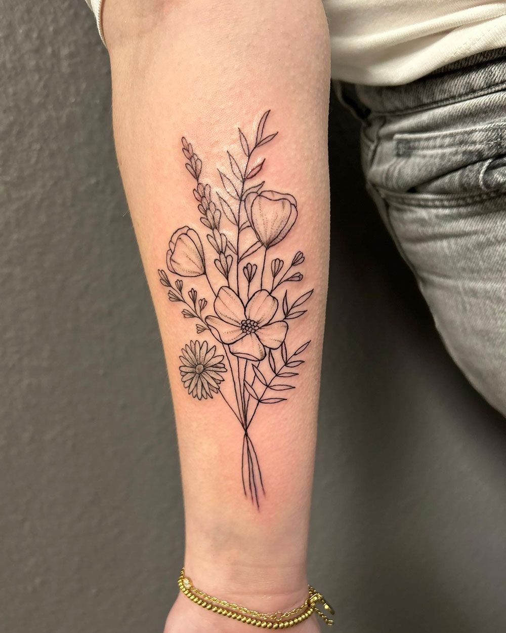Eine Frau hat eine Tätowierung mit einem Blumenstrauß auf ihrem Unterarm.