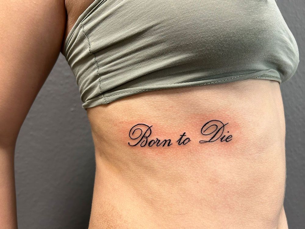 Eine Frau hat auf ihrer Seite eine Tätowierung mit der Aufschrift „Born to Die“.