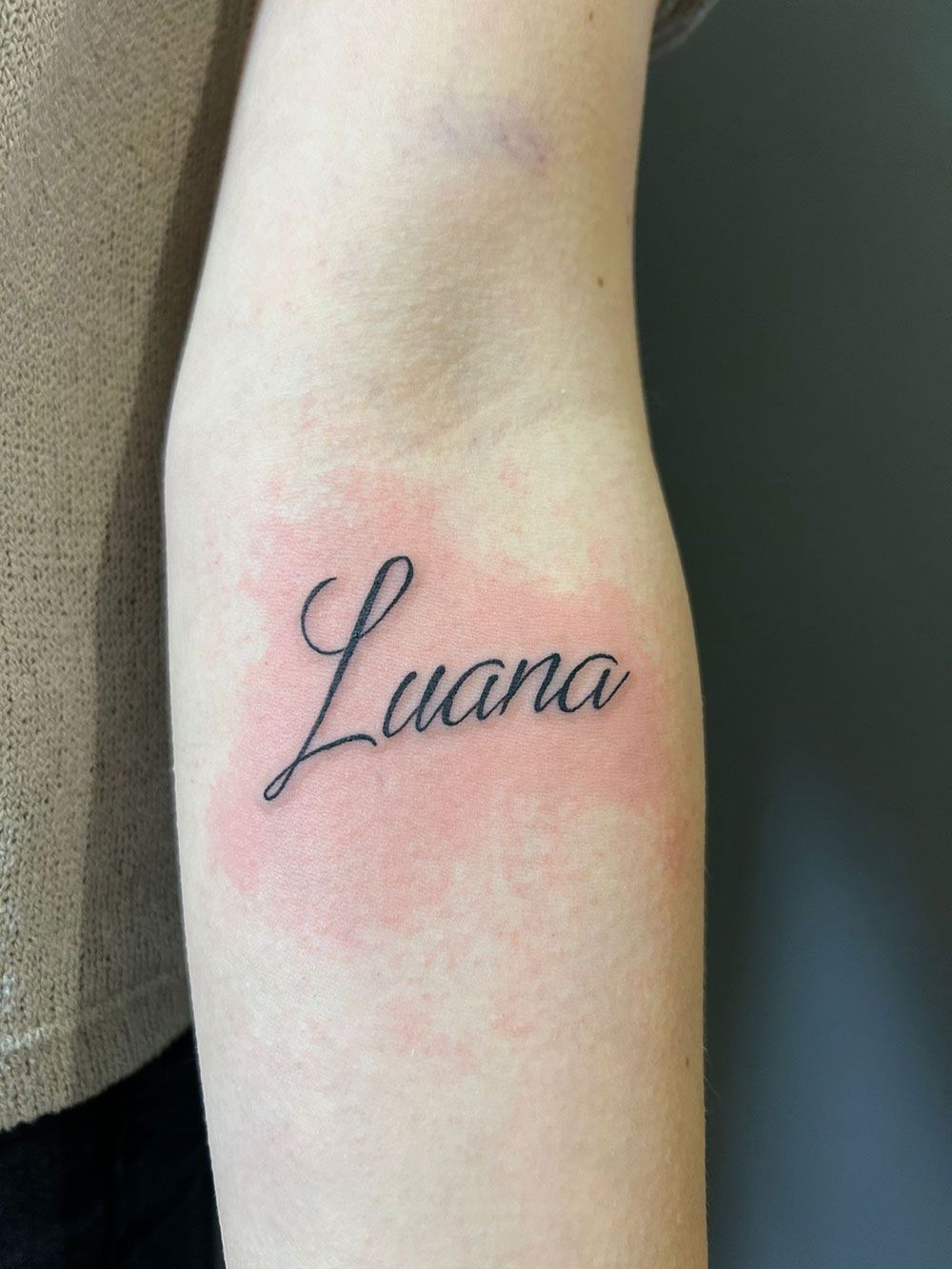 Eine Frau hat eine Tätowierung mit dem Namen Luana auf ihrem Arm.