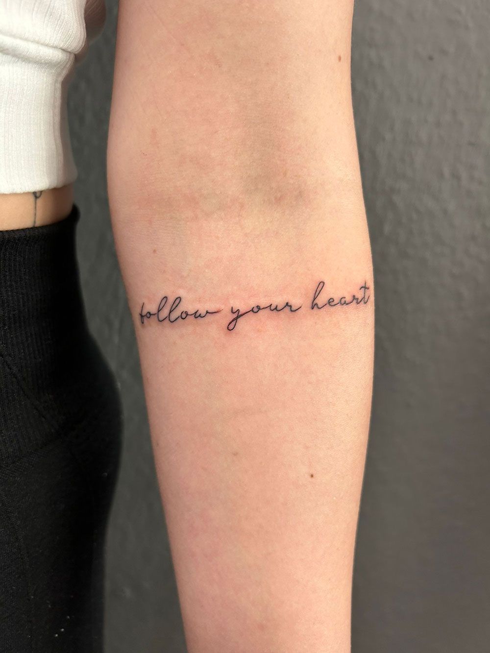 Eine Frau hat eine Tätowierung auf ihrem Unterarm mit der Aufschrift „Folge deinem Herzen“.